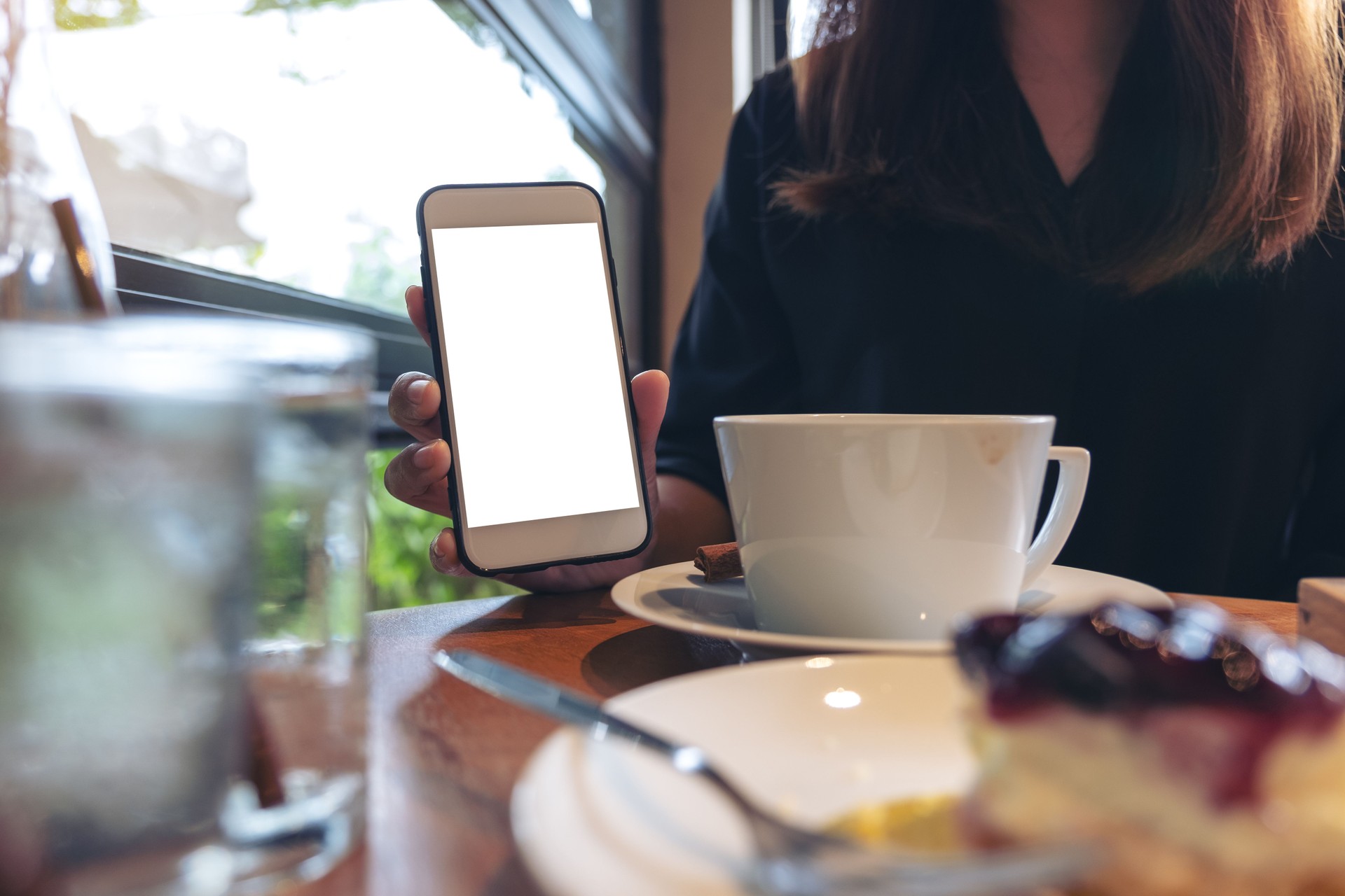 Image de la maquette d’une femme tenant et montrant blanc téléphone portable avec un écran blanc avec café et gâteau sur la table à café